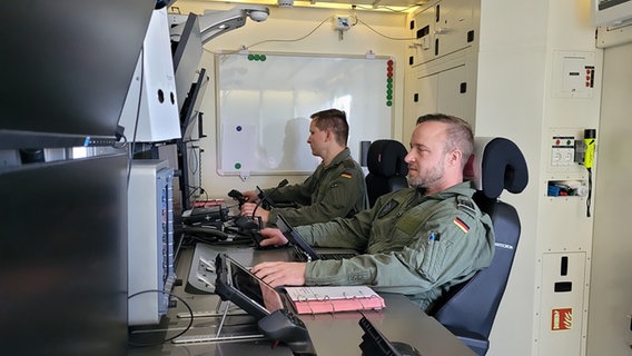 Zwei Bundeswehrsoldaten sitzen in einem mobilen Raum mit Steuereinheiten für die neue Heron-Drohne. © NDR Foto: Frank Goldenstein