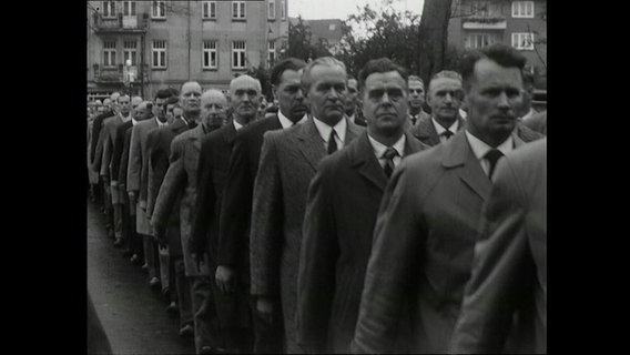 Eine Schwarzweiß-Aufnahme von mehreren Personen die in einer Reihe stehen © NDR Foto: NDR Screenshot