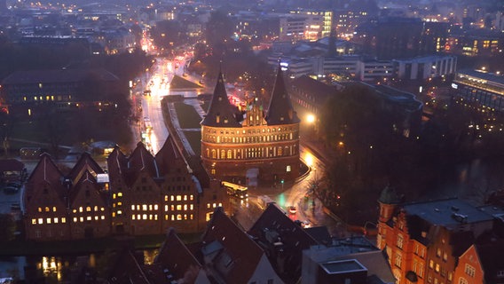 Das beleuchtete Holstentor in Lübeck in abendlicher Stimmung mit vorbeifahrenden Autos © Ursula Andresen Foto: Ursula Andresen