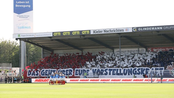 Im Holsteinstadion findet sich die Fußballmannschaft ein. Auf den Tribühnen jubeln die Fans. © picture alliance/dpa Foto: Claus Bergmann