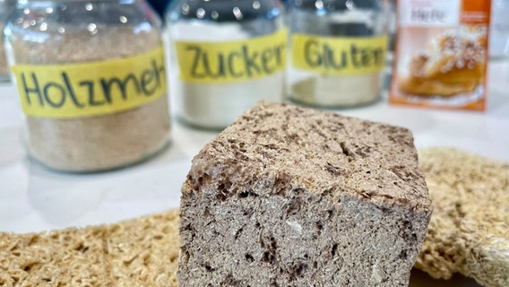 Holzschaumstoff liegt auf dem Tisch, im Hintergrund die Zutaten, um ihn zu herzustellen. © NDR Foto: Naïs Marie Baier