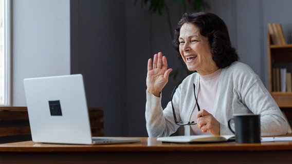 Eine ältere Dame grüßt jemanden in einer Videokonferenz. © Imago Zoonar 