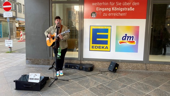 Ein junger Mann singt an einer Straßenecke mit seiner Gitarre und einem Verstärker. © Linda Ebener / NDR Foto: Linda Ebener / NDR