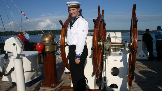 Matrosin Jenny Böken steht vor dem Steuerrad des Segelschiffs Gorch Fock. © Uwe Böken Foto: Uwe Böken
