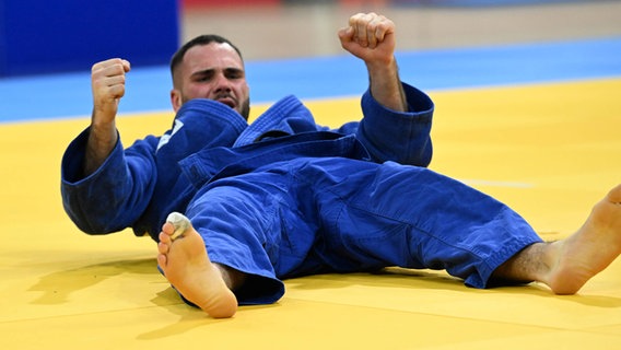 Ein Mann in einem blauen Karate-Anzug liegt auf dem Boden und reckt die Fäuste in die Luft © imago images Foto: Ralf Kuckuck