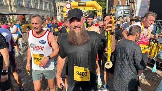 Ein Mann präsentiert nach einem Marathon seine Medaille © NDR Foto: Ole ter Wey