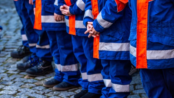 Kinder in Feuerwehruniform stehen auf einem Platz in einer Reihe, man sieht nur einen Ausschnitt ihrer Jacken und Hände. © picture alliance / dpa / Jens Büttner Foto: Jens Büttner