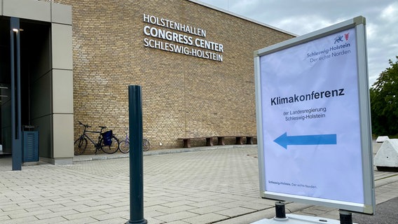 Der Eingang der Holstenhallen, vor denen ein Schild mit dem Hinweis "Klimakonferenz" steht. © NDR Foto: Fabian Boerger