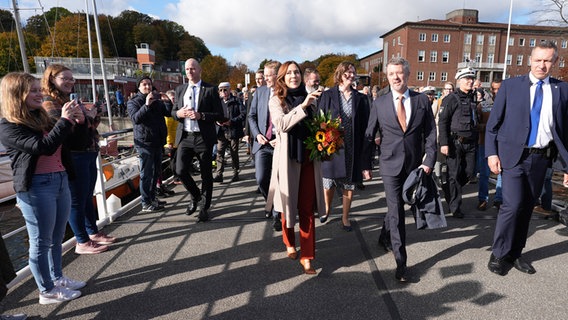 König Frederik X. von Dänemark und Königin Mary von Dänemark gehen mit Daniel Günther (CDU) zum Fähranleger Reventloubrücke in Kiel. © dpa-Bildfunk Foto: Marcus Brandt