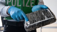 Ein Polizeibeamter öffnet ein Drogenpaket mit weißem Pulver. © picture alliance / dpa | Paul Zinken Foto: Paul Zinken