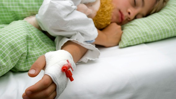 Ein Junge (10) liegt mit einem Kuscheltier im Arm und einem Zugang an der Hand im Krankenbett. © picture alliance / imageBROKER Foto: Michaela Begsteiger