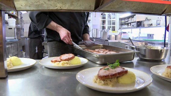 Eine Köchin serviert einen Kassler auf Kartoffelbrei in einer Gastro-Küche. © NDR 