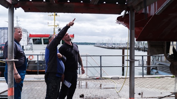 Drei Männer stehen vor dem zu wartenden Lotsenboot. Einer der Männer zeigt auf eine Stelle am Boot, während die anderen beiden ihm aufmerksam zuhören. © NDR Foto: Dominik Dührsen