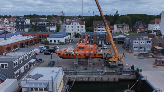 Das orangene Lotsenboot wird mit einem großen Kran aus dem Wasser geholt. © NDR Foto: Dominik Dührsen