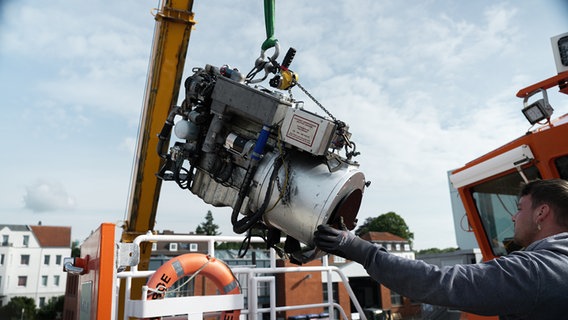 Der Dieselgenerator des Lotsenbootes hängt an einem Kran und wird von einem Mann mit seiner Hand geführt. © NDR Foto: Dominik Dührsen