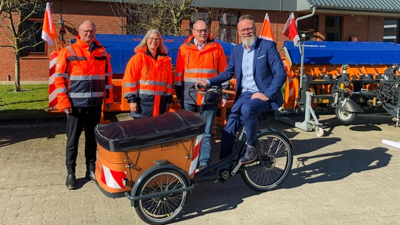 Schleswig-Holsteins Wirtschaftsminister Claus Ruhe Madsen (CDU) sitzt auf einem Lastenrad, neben ihm stehen drei weitere Personen. © NDR Foto: Birte Steuer