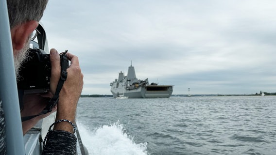 Ein Mann fotografiert ein Marineschiff von einem anderen Boot aus. © NDR Foto: Tobias Gellert
