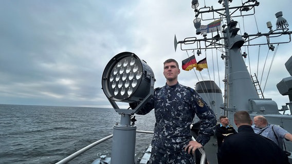 Ein Mann in einem Marineoverall steht an Deck eines Marineschiffes und bedient einen Scheinwerfer © NDR Foto: Andreas Schmidt