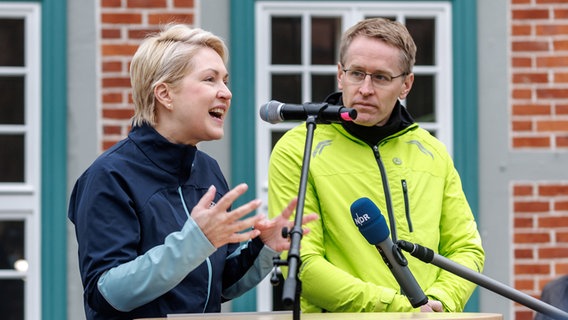 Mecklenburg-Vorpommerns Ministerpräsidentin Manuela Schwesig (SPD) spricht neben Schleswig-Holsteins Ministerpräsident Daniel Günther (CDU) vor Beginn des Grenzlaufs zum Jahrestag des Mauerfalls auf dem Marktplatz von Boizenburg. © dpa Foto: Markus Scholz