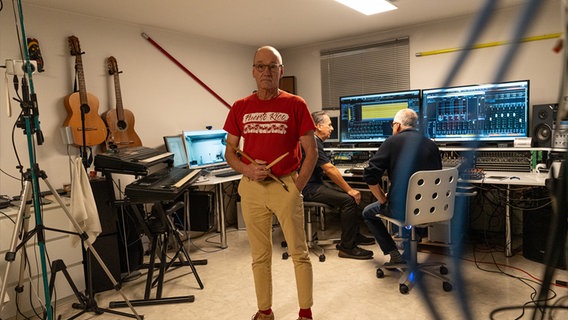 Ein Mann in rotem T-Shirt steht mit Schlagzeugknüppeln in einem Tonstudio. © NDR Foto: Dominik Dührsen