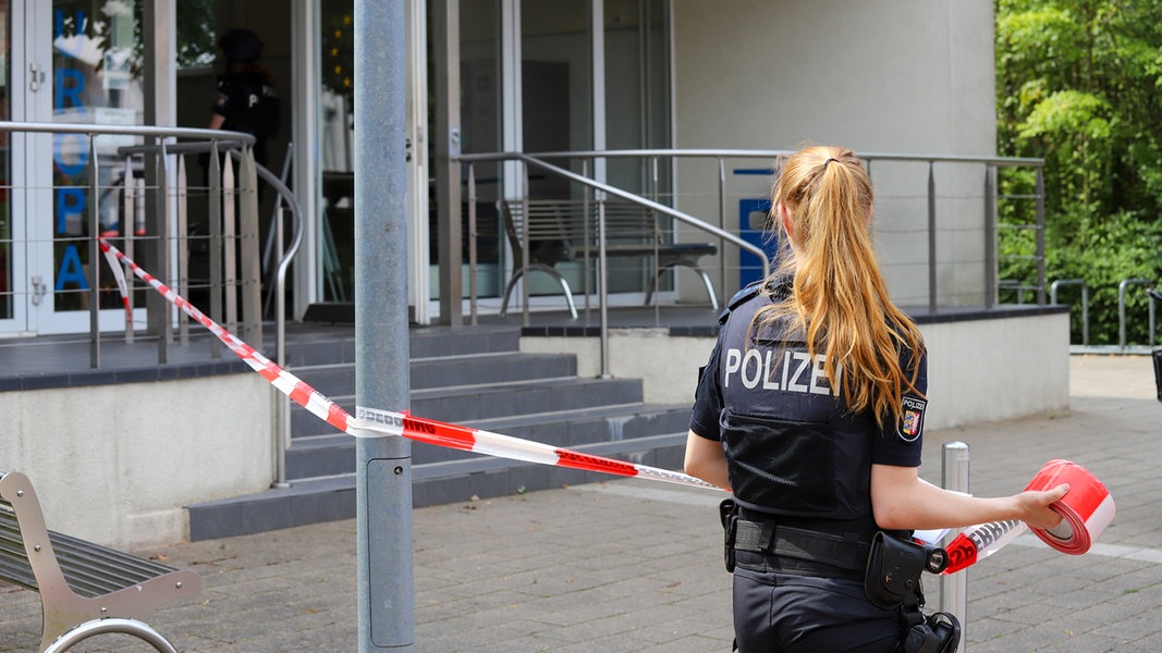 Eine Polizistin sperrt den Eingang zu einer Schule mit einem rotweißen Absperrband ab