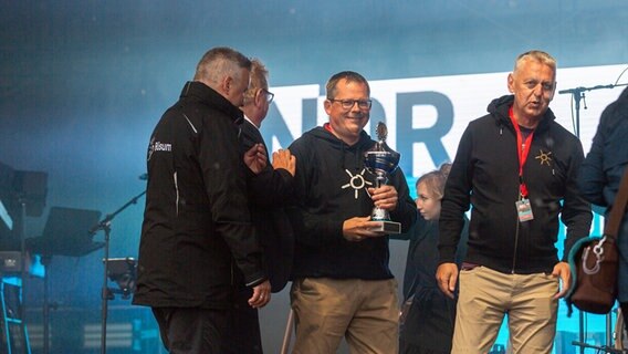 Mehrere Männer stehen auf einer Bühne, einer von ihnen hält einen Pokal in Händen. © NDR Foto: Dominik Dührsen