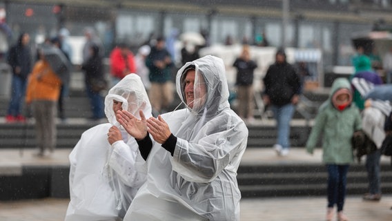 Ein Mann und eine Frau stehen in Regencape vor einer Bühne. © NDR Foto: Dominik Dührsen