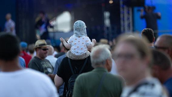 Kleines Kind mit einem weiße Hut und weißem T-Shirt sitzt auf den Schultern eines Mannes. © NDR Foto: Dominik Dührsen
