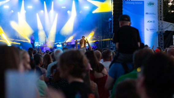 Menschen von hinten vor einer großen Bühne mit blauem Hintergund. © NDR Foto: Dominik Dührsen