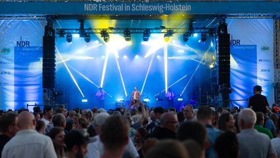 Große blaue Bühne mit einem Sänger in einem braunen Hemd. Davor stehen tausende Menschen. © NDR Foto: Dominik Dührsen