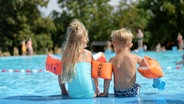 Zwei Kinder sitzen mit Schwimmflügeln am Rand eines Freibads. © dpa-Bildfunk Foto: Frank May