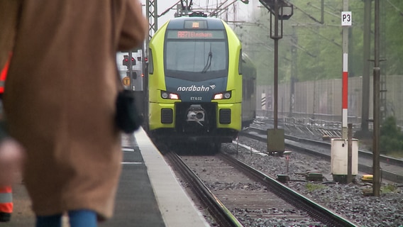 Menschen stehen am Bahngleis während ein Zug der Nordbahn fährt ein. © NDR 