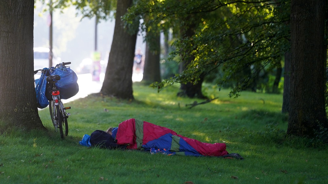 Ein Obdachloser liegt auf einer Wiese in seinem Schlafsack neben seinem Fahrrad.