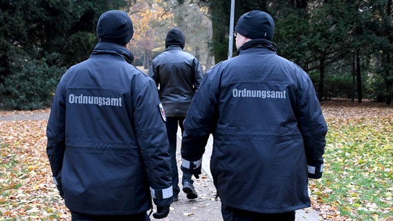 Zwei Beamte des Ordnungsamtes laufen durch einen Park einem Mann hinterher. © dpa | Bildfunk Foto: Carmen Jaspersen