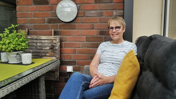 Petra Gehlhaar sitzt auf ihrer Terrasse und lächelt in die Kamera. © NDR Foto: Lisa Pandelaki