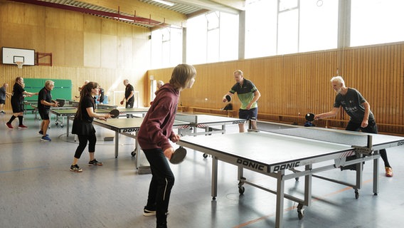 Eine Gruppe Menschen spielt Tischtennis in einer Sporthalle. © NDR Foto: Lisa Pandelaki