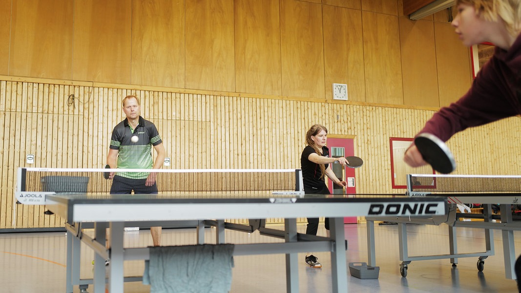 Eine Gruppe Menschen spielt Tischtennis in einer Sporthalle.