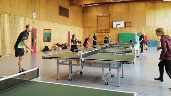 Eine Gruppe Menschen spielt Tischtennis in einer Sporthalle. © NDR Foto: Lisa Pandelaki