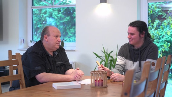 Zwei Personen sitzen an einem Tisch und unterhalten sich © NDR Foto: NDR Screenshot