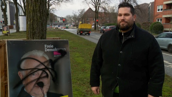 Florian Meyer, Kreisvorsitzender der FDP Neumünster, steht neben einem beschmierten Wahlplakat. © NDR 