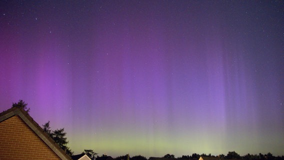 Zwischen den Dächern von Kaltenkirchen schimmern grün violette Polarlichter. © NDR Foto: Erik Wischnewski