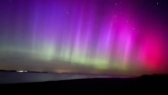 Die nächtlichen Polarlichter schimmern in einem grün-violett Farbton über dem Wasser in Noer. © NDR Foto: Dominik Dührsen