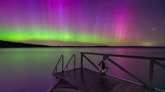 Ein Steg wird von grün violetten Polarlichtern angestrahlt. © Christoph Andresen Foto: Christoph Andresen