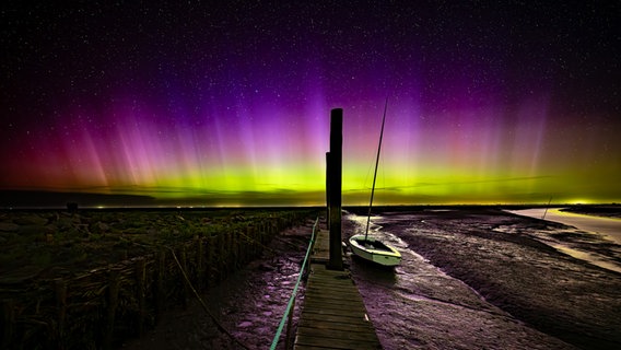 Ein Boot liegt bei Ebbe auf dem Grund und wird durch die hellen Polarlichter beleuchtet. © Henrik Busse Foto: Henrik Busse