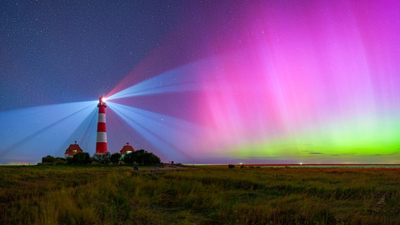 Ein rot-weiß gestreifter Leuchtturm, der in Betrieb ist, wird von violett grünen Polarlichtern angeschienen. © Mike Mohr Foto: Mike Mohr