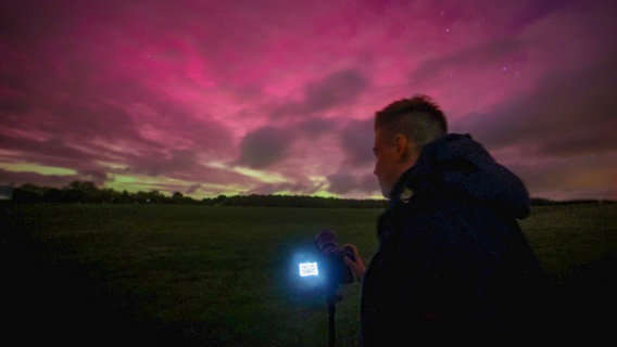 Ein junger Mann fotografiert mit seiner Kamera den Nachthimmel, der von Polarlichtern erleuchtet wird. © EHL Media Foto: Tim Meyer