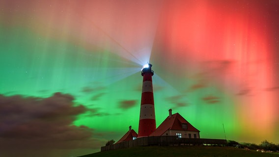 Am Himmel leuchten bunte Polarlichter und Lichter des Leuchtturms Westerheversand. © Mike Mohr Foto: Mike Mohr