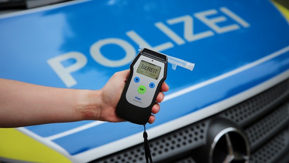 Ein Polizist hält ein einsatzbereites Atemtestgerät vor der Motorhaube eines Streifenwagens. © NDR Foto: Pavel Stoyan