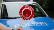 Ein Polizist hält eine Polizeikelle vor einem Streifenwagen. © NDR Foto: Pavel Stoyan