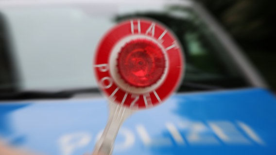 Ein Polizist hält eine Polizeikelle vor einem Streifenwagen. © NDR Foto: Pavel Stoyan